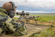 Sportschütze mit Tarnjacke zielt mit Gewehr und Zielfernrohr auf Ziel in freier Natur